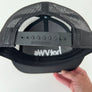 Close-up of the back of a black mesh trucker hat held by a hand, showing a black adjustable strap with RICHARDSON branding and a white logo printed on the inside.