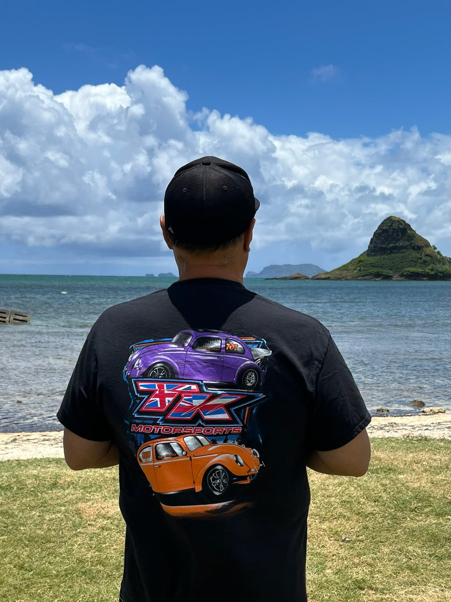 Person wearing a black t-shirt with car graphics by a scenic waterfront.