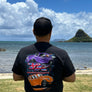 Person wearing a black t-shirt with car graphics by a scenic waterfront.