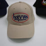 A beige baseball cap with an embroidered oval logo reading 'hotVWs magazine' in blue and red, displayed on a white surface with two other branded caps partially visible in the background.