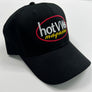 A black baseball cap with an embroidered oval logo on the front panel. The logo features the words 'Hot Magazine' in white and yellow, outlined in red.