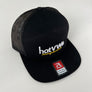 A black trucker hat with a black mesh back and a flat brim, featuring 'hotvwe merch' embroidered in white and yellow on the front. A red and white Richardson Flat Bill Snapback sticker is visible on the brim.
